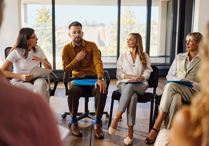 A group of people sat talking in a circle in a work setting. 