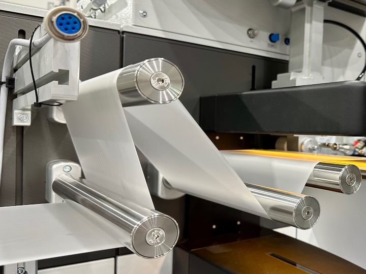 Polymer extrusion services illustrated by a machine producing plastic films that are wound around metal cylinders on a machine