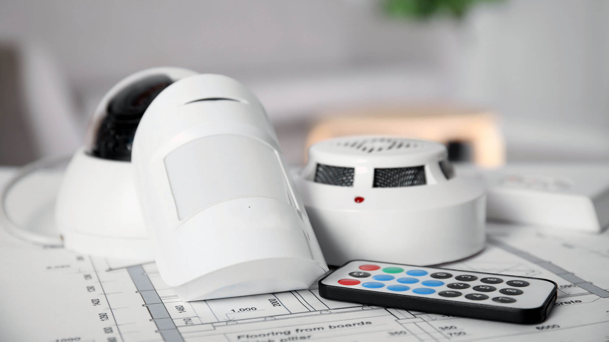 CCTV camera, remote control, smoke and movement detectors on building plan indoors. Home security system 